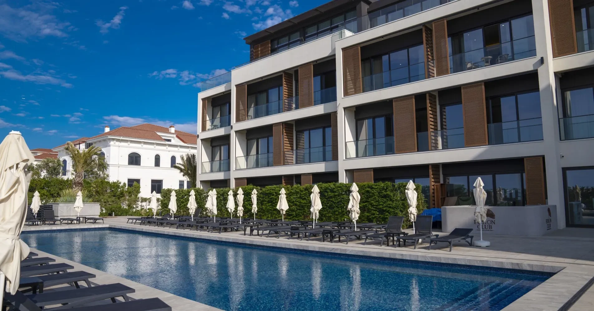 Двор White Residences: бассейн с шезлонгами вдоль корпуса; справа у бассейна — табличка Fusion Club